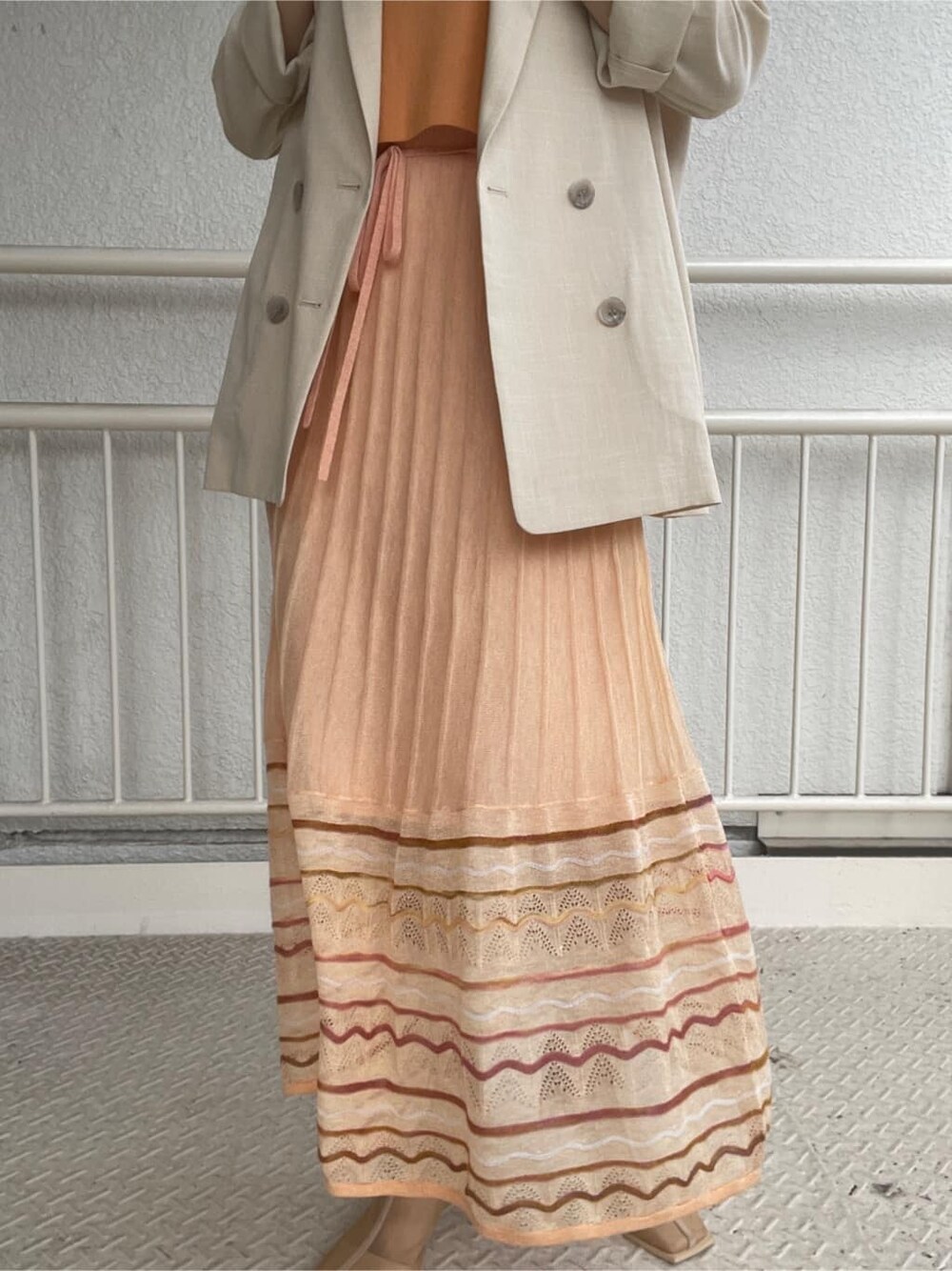 ベージュ系のブーツ、ベージュ系のテーラードジャケット、オレンジ系のワンピースを着用したレディースの春コーディネートの10枚目の写真