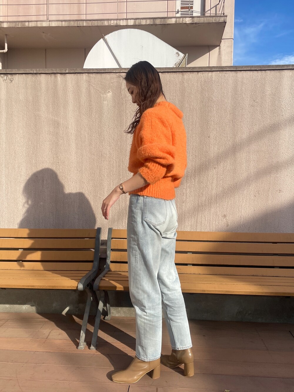 ブルー系のデニムパンツ、オレンジ系のニット/セーター、ベージュ系のブーツを着用したレディースの冬コーディネートの4枚目の写真