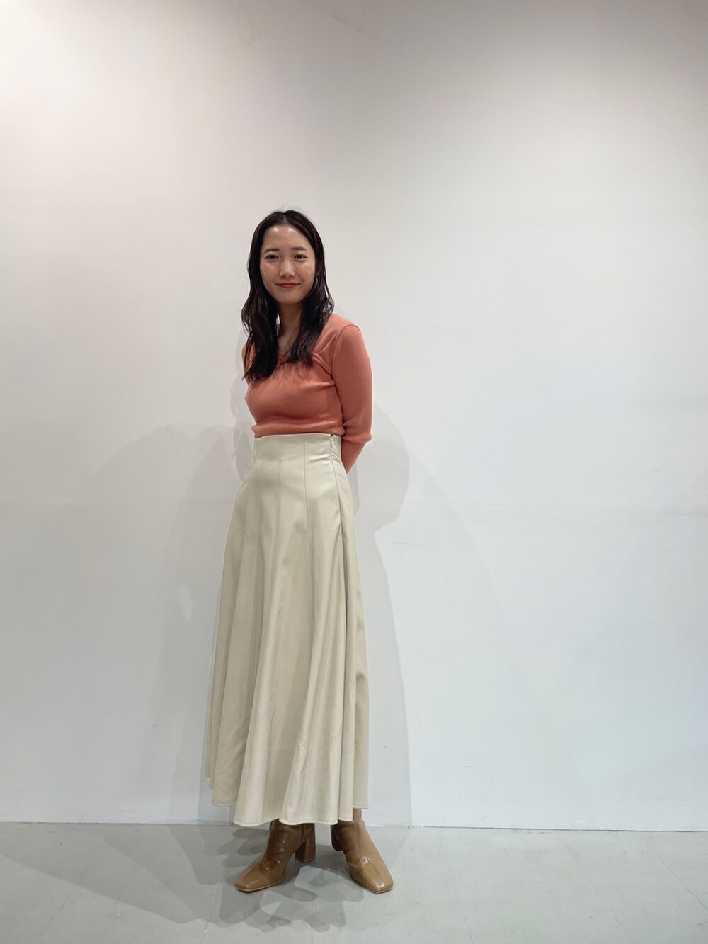 オレンジ系のニット/セーター、ホワイト系のスカート、ベージュ系のブーツを着用したレディースの秋コーディネートの5枚目の写真