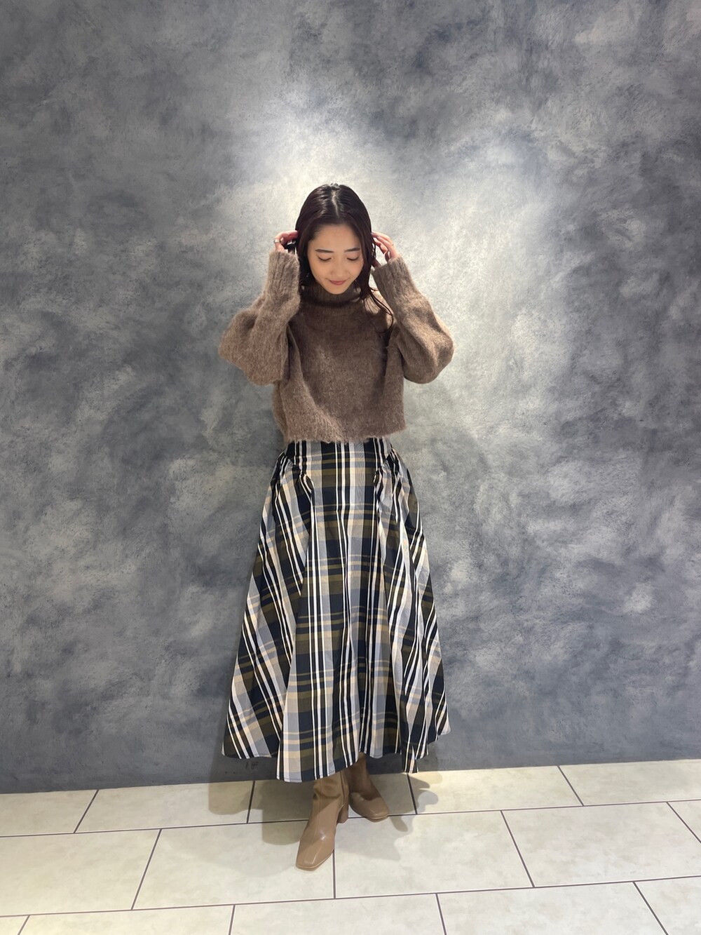 ブラウン系のニット/セーター、オレンジ系のスカート、ベージュ系のブーツを着用したレディースの秋コーディネートの2枚目の写真