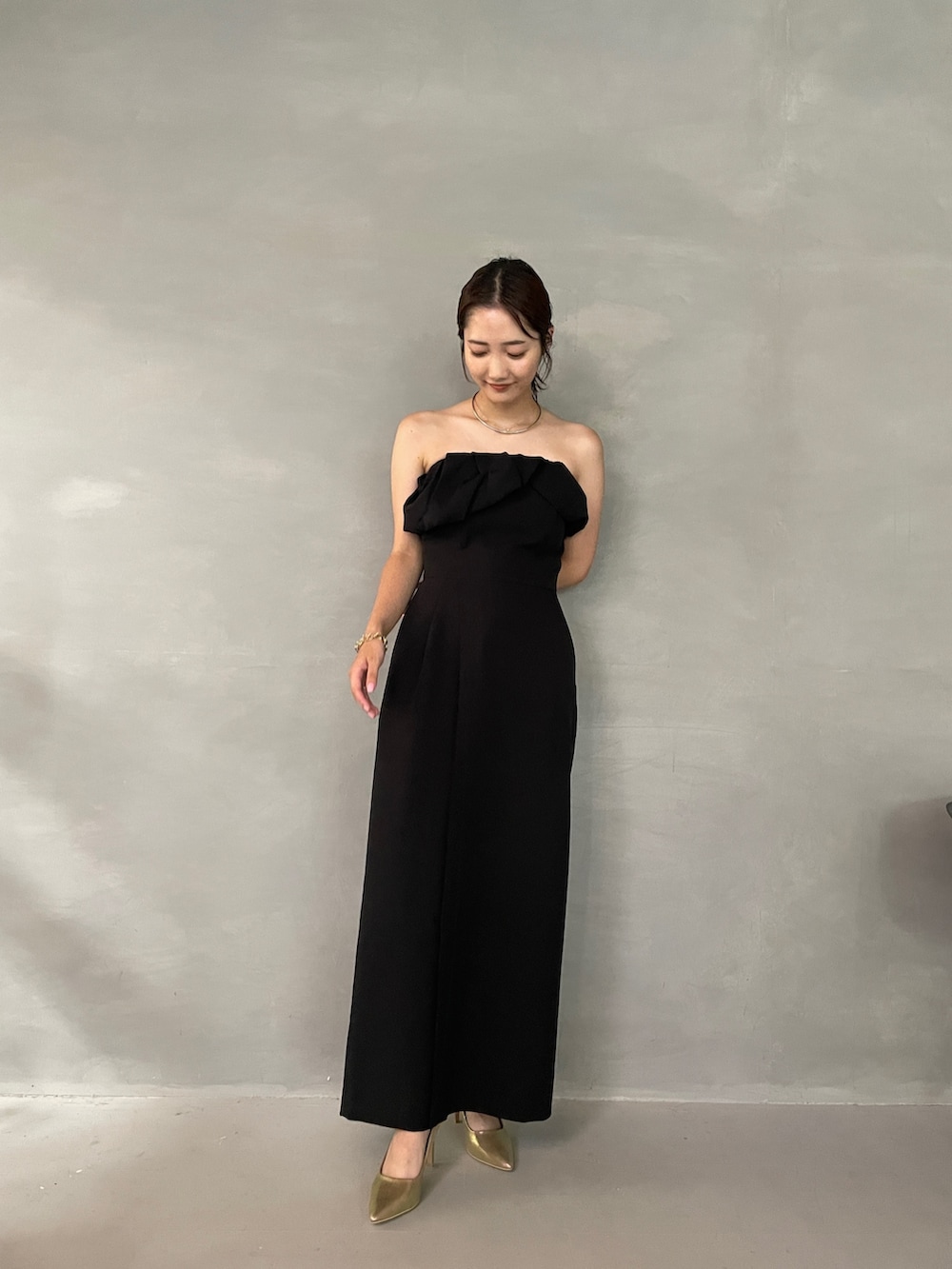 ゴールド系のパンプス、ブラック系のパンツドレス、シルバー系のチョーカーを着用したレディースの夏コーディネートの3枚目の写真
