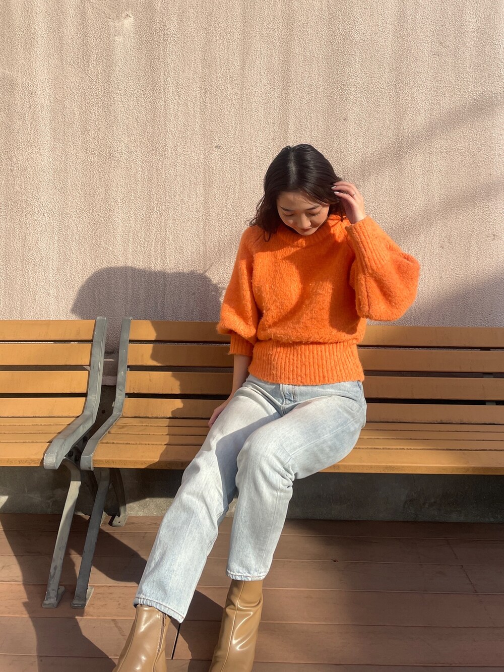 ブルー系のデニムパンツ、オレンジ系のニット/セーター、ベージュ系のブーツを着用したレディースの冬コーディネートの5枚目の写真