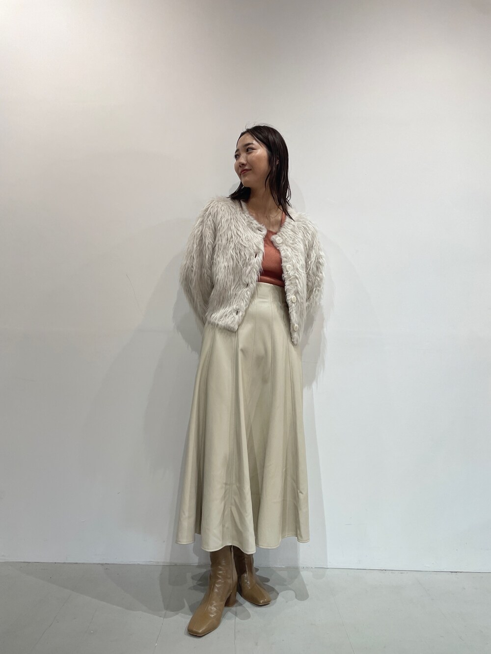 ホワイト系のスカート、ベージュ系のブーツ、オレンジ系のニット/セーターを着用したレディースの夏コーディネートの2枚目の写真