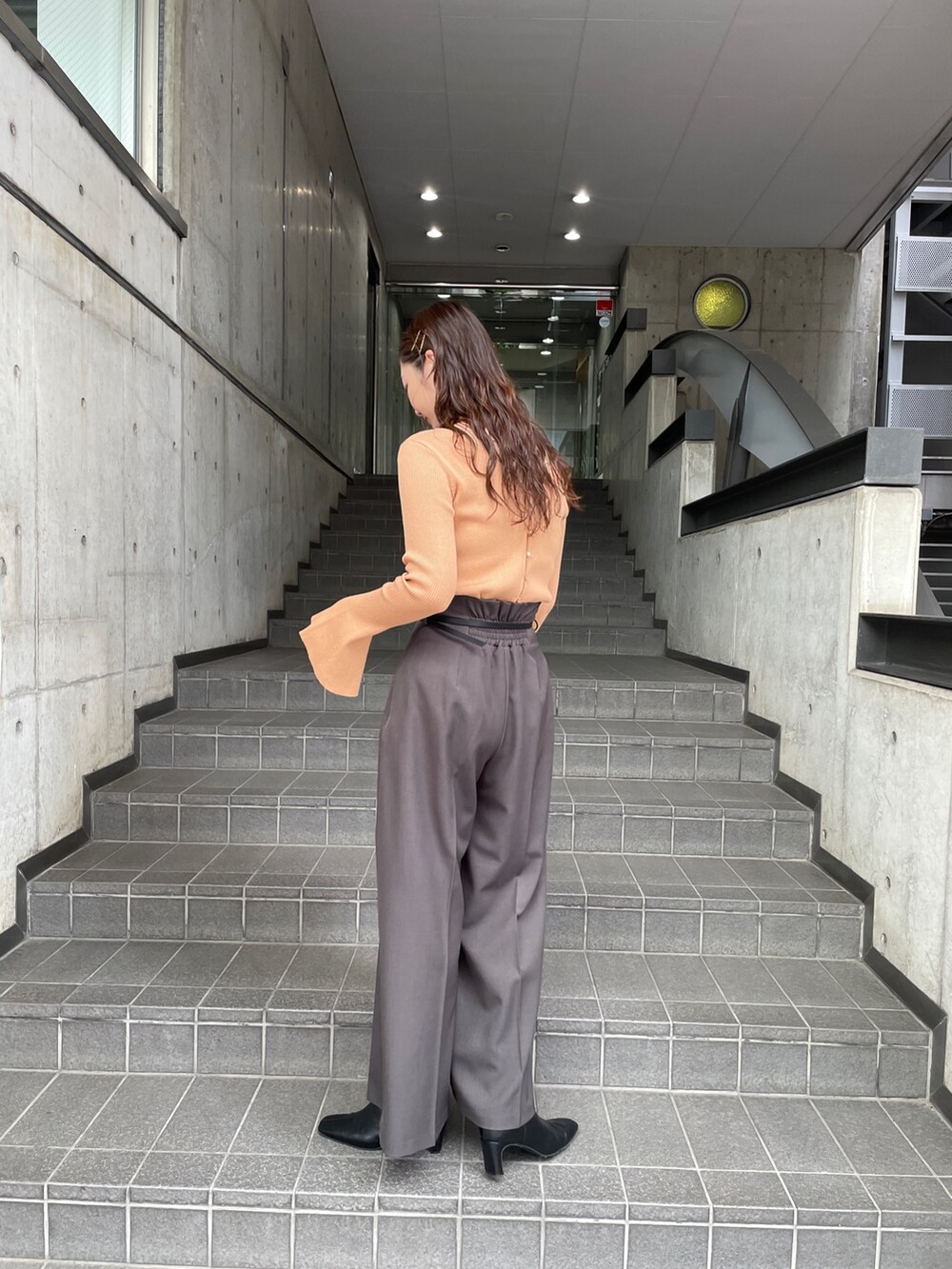 グレー系のその他パンツ、オレンジ系のニット/セーター、ブラック系のブーツを着用したレディースの秋コーディネートの4枚目の写真