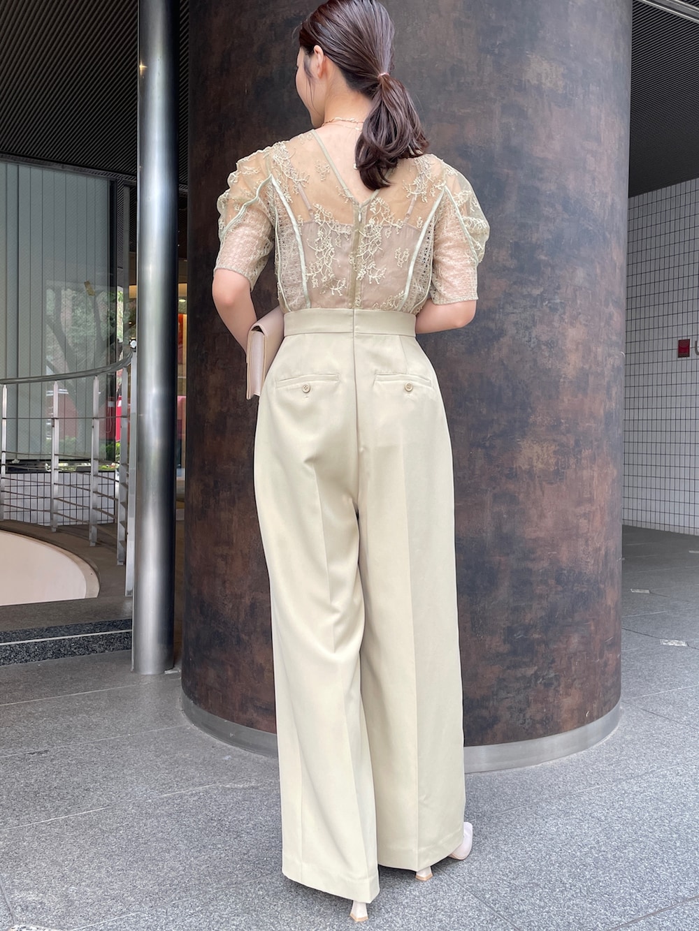 グリーン系のパンツドレス、ベージュ系のクラッチバッグ、ベージュ系のパンプスを着用したレディースの冬コーディネートの6枚目の写真