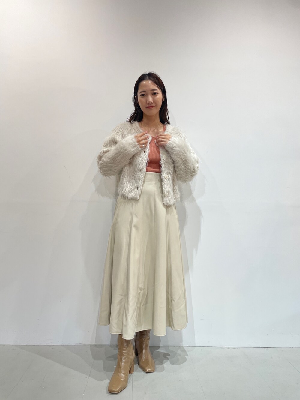 ホワイト系のスカート、ベージュ系のブーツ、オレンジ系のニット/セーターを着用したレディースの夏コーディネートの4枚目の写真