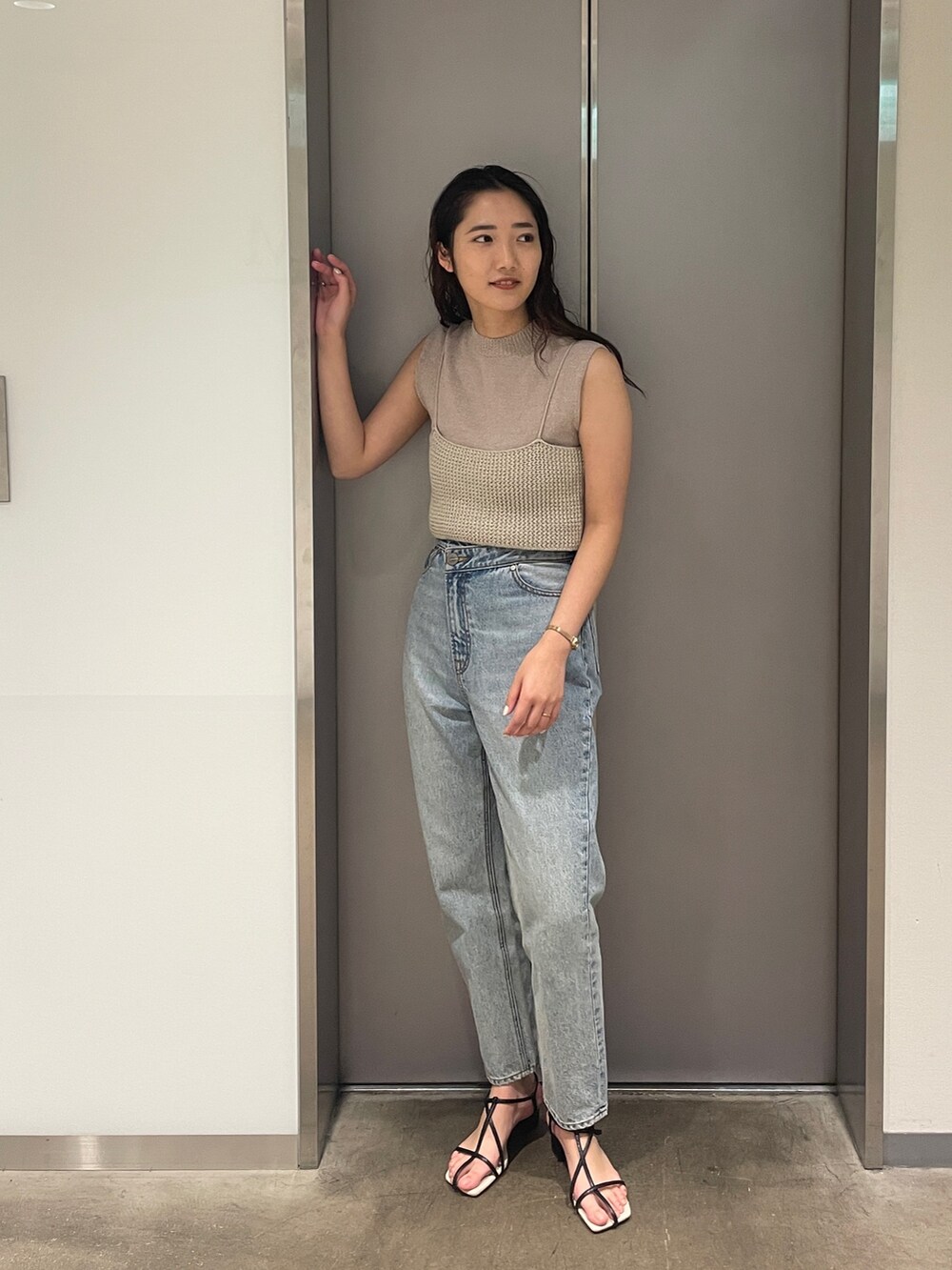 ブルー系のデニムパンツ、ベージュ系のニット/セーター、ブラック系のサンダルを着用したレディースの春コーディネートの2枚目の写真