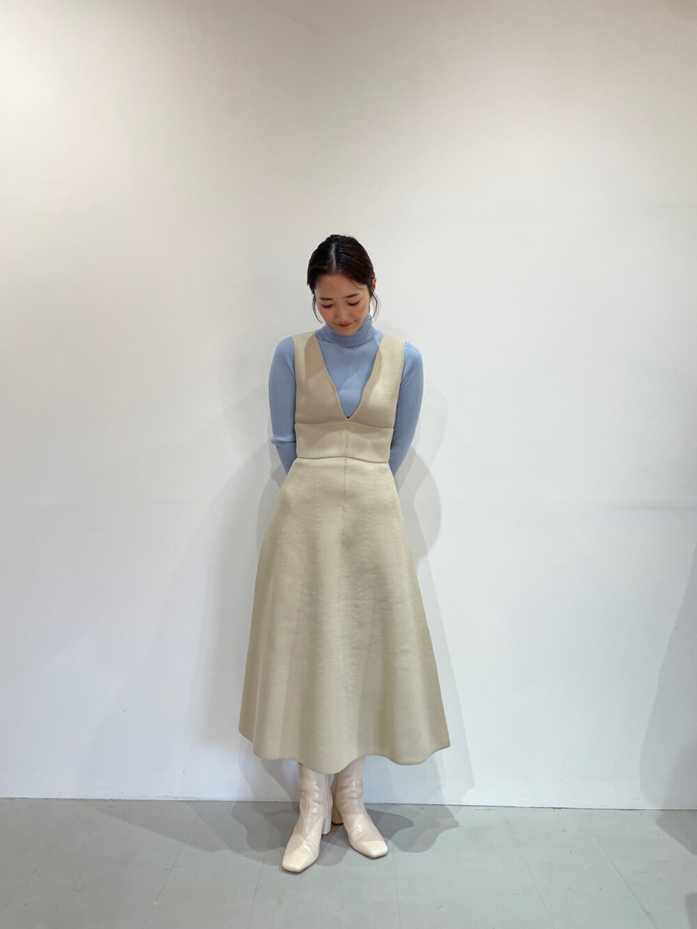 ブルー系のニット/セーター、ホワイト系のジャンパースカート、ホワイト系のブーツを着用したレディースの夏コーディネートの6枚目の写真