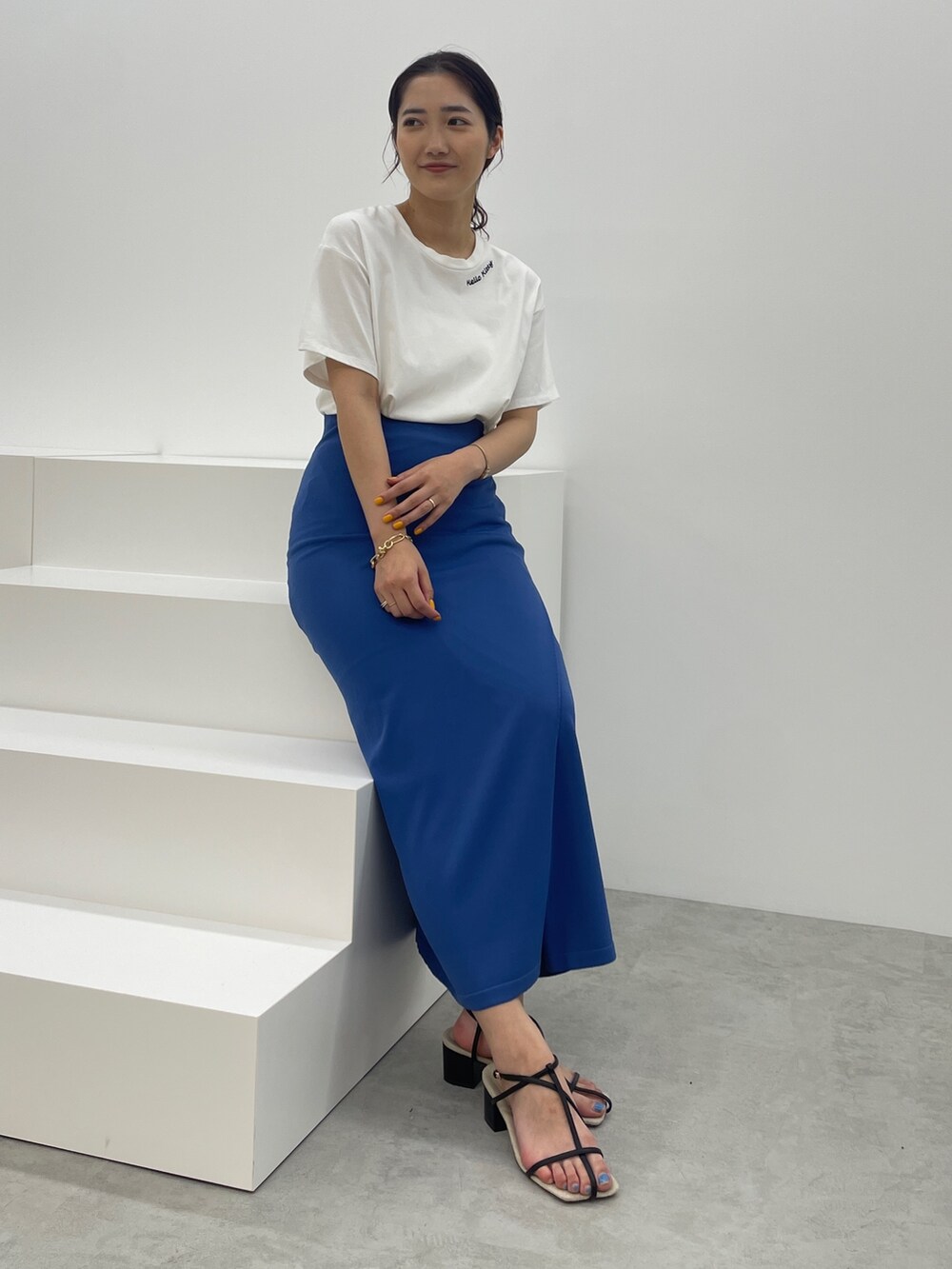 ブルー系のスカート、ホワイト系のTシャツ/カットソー、ブラック系のサンダルを着用したレディースの春コーディネートの3枚目の写真