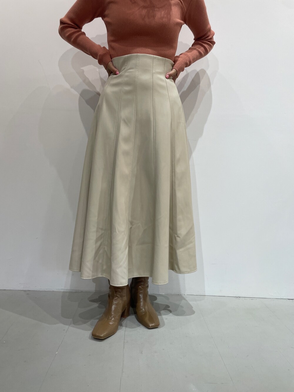 オレンジ系のニット/セーター、ホワイト系のスカート、ベージュ系のブーツを着用したレディースの夏コーディネートの7枚目の写真