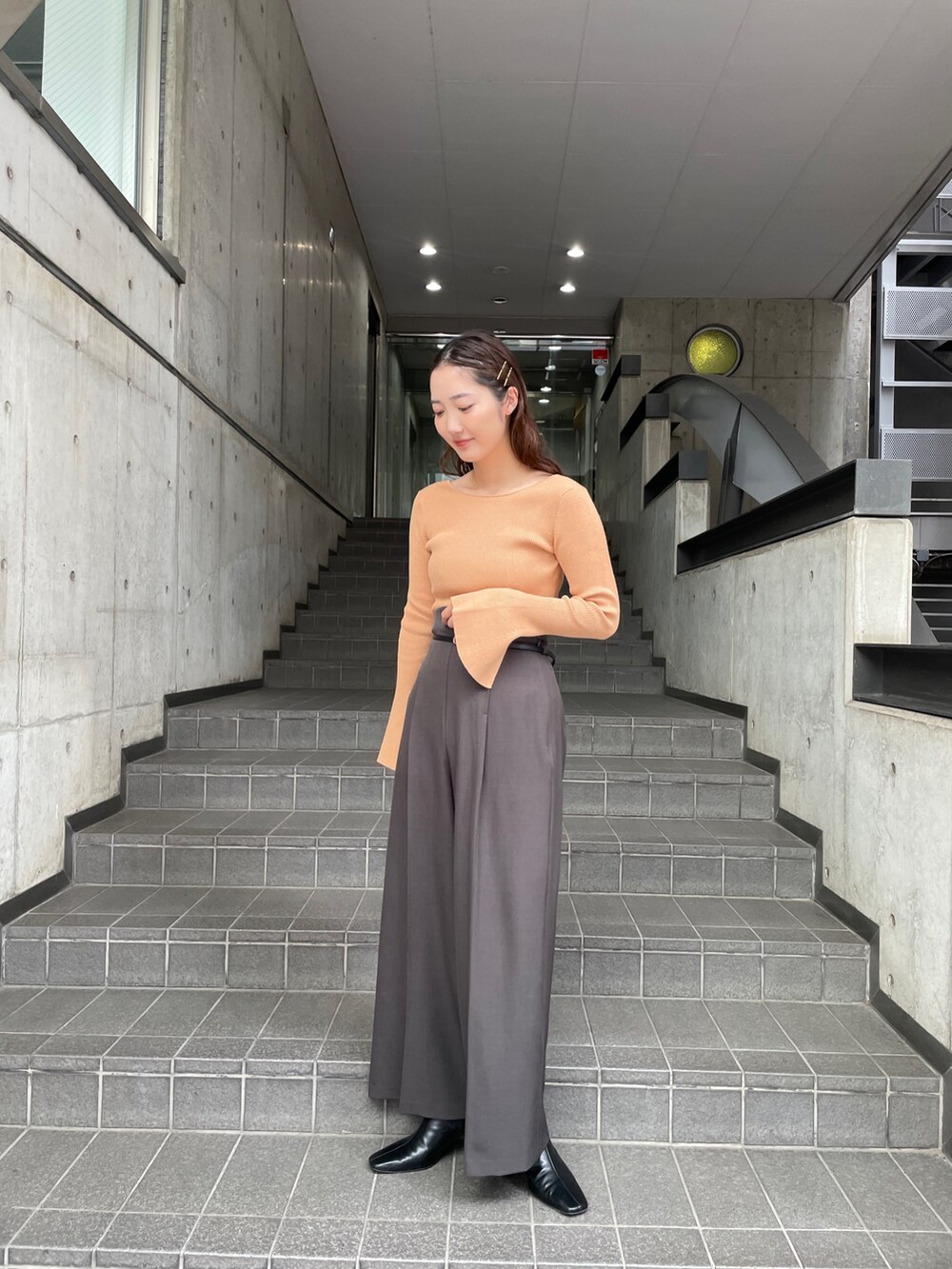 グレー系のその他パンツ、オレンジ系のニット/セーター、ブラック系のブーツを着用したレディースの秋コーディネートの2枚目の写真