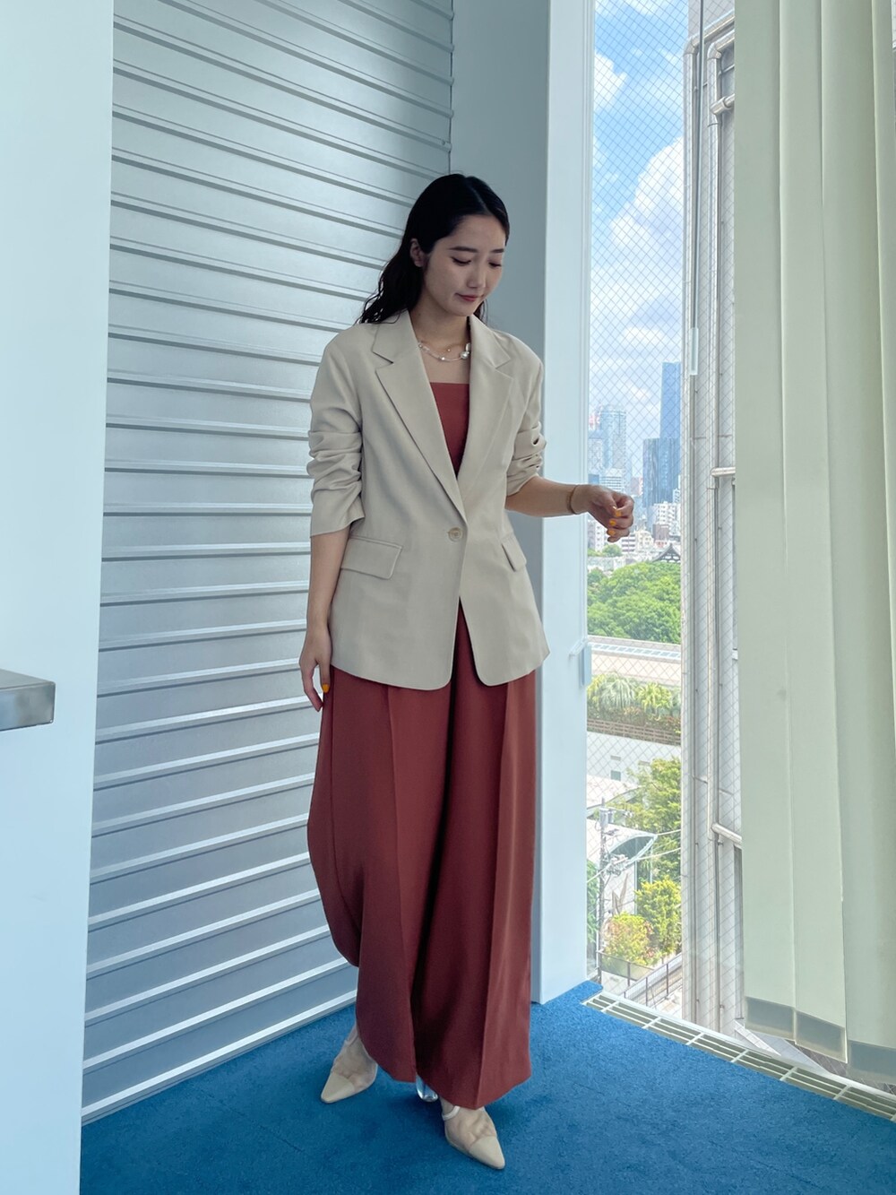 ベージュ系のパンプス、オレンジ系のパンツドレス、ベージュ系のテーラードジャケットを着用したレディースの夏コーディネートの2枚目の写真