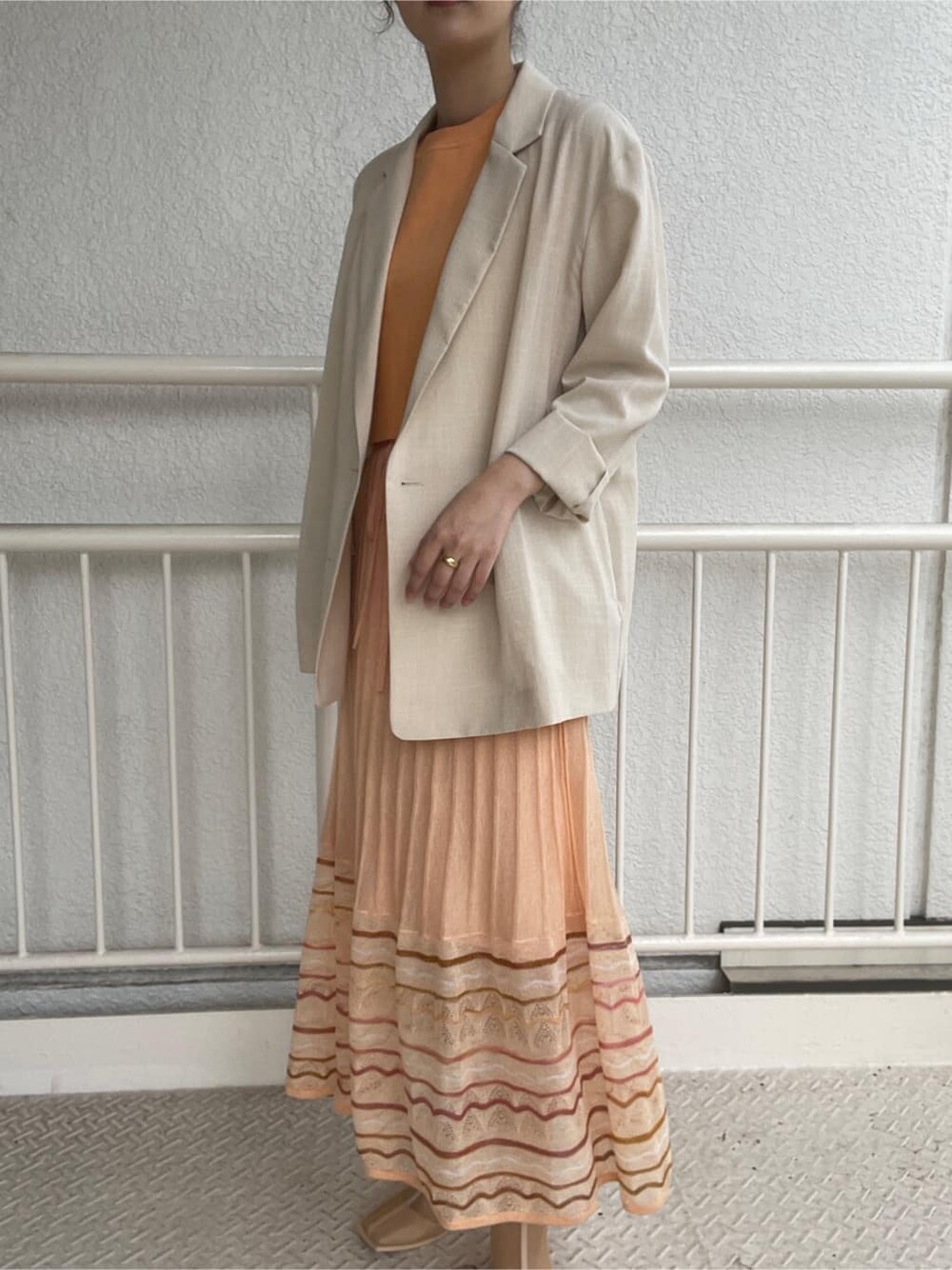 ベージュ系のブーツ、ベージュ系のテーラードジャケット、オレンジ系のワンピースを着用したレディースの春コーディネートの2枚目の写真