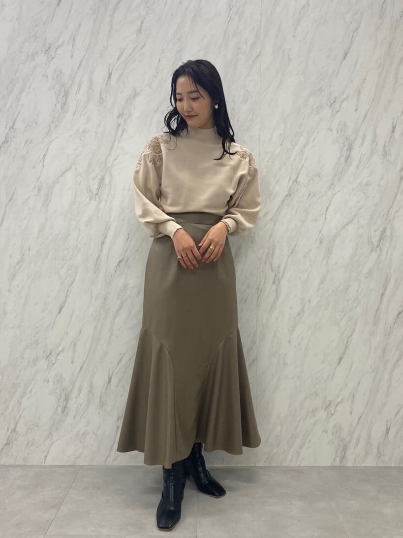 ブラック系のブーツ、ベージュ系のスカート、ホワイト系のニット/セーターを着用したレディースの秋コーディネートの2枚目の写真