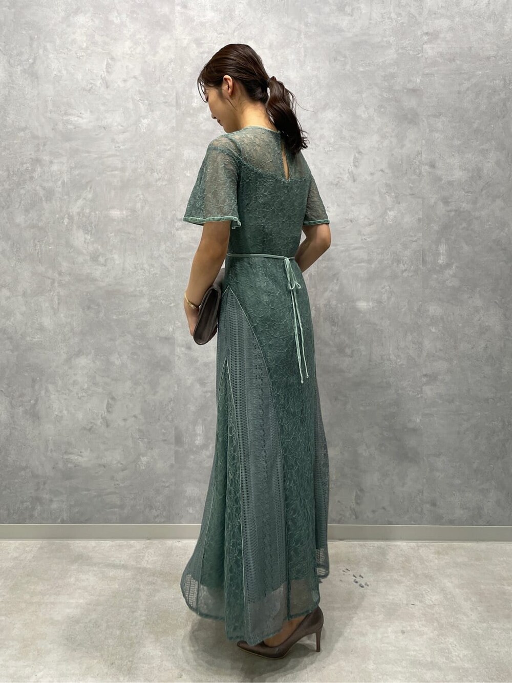 シルバー系のパンプス、シルバー系のクラッチバッグ、グリーン系のドレスを着用したレディースの夏コーディネートの6枚目の写真