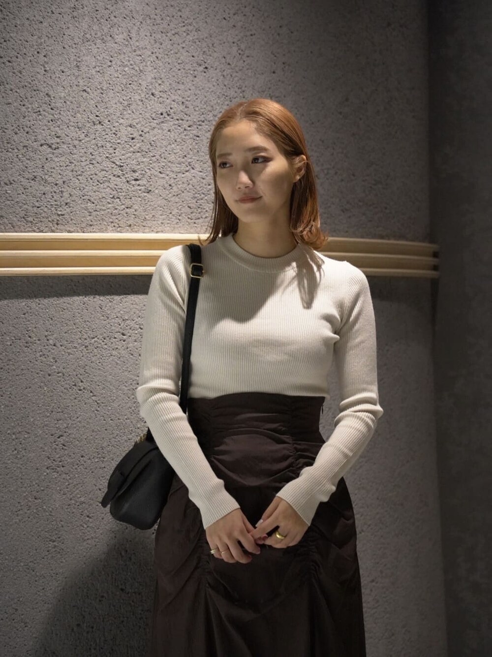 ブラック系のショルダーバッグ、ブラウン系のスカート、ホワイト系のニット/セーターを着用したレディースの秋コーディネートの7枚目の写真