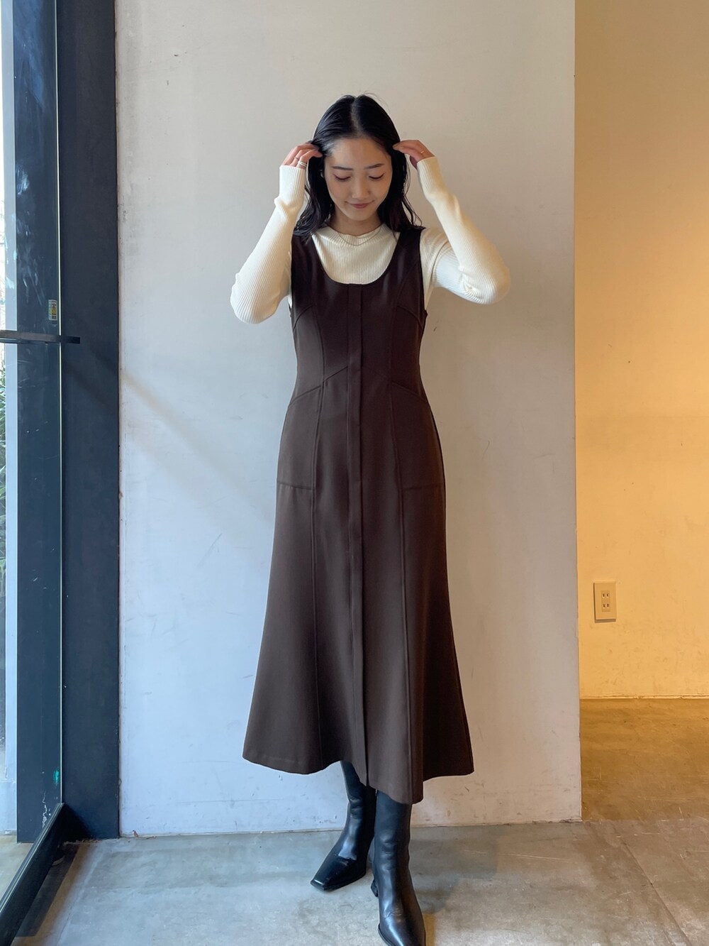 ブラック系のブーツ、ホワイト系のニット/セーター、ブラウン系のジャンパースカートを着用したレディースの冬コーディネートの2枚目の写真