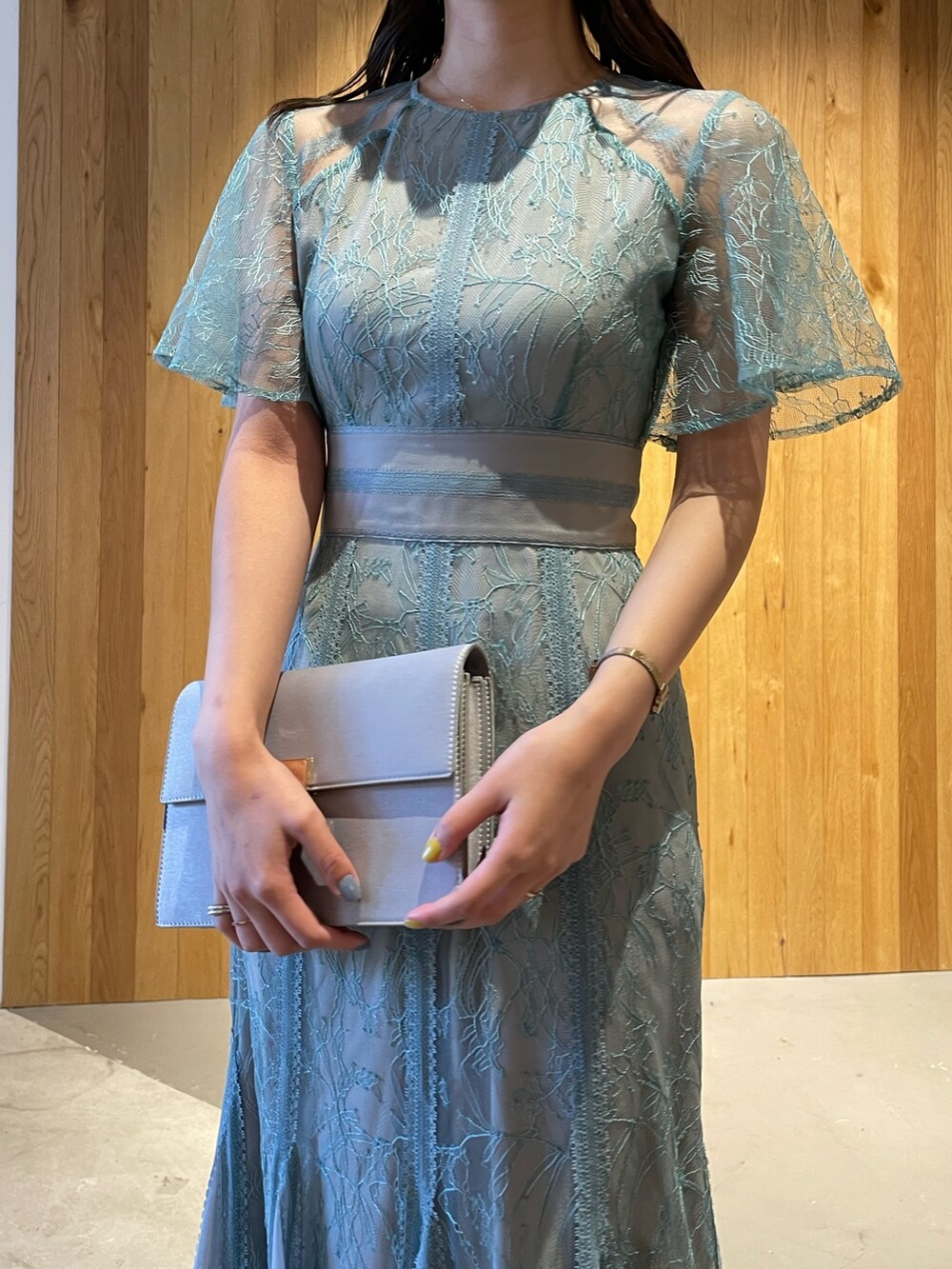 グレー系のクラッチバッグ、グレー系のパンプス、グリーン系のドレスを着用したレディースの冬コーディネートの5枚目の写真