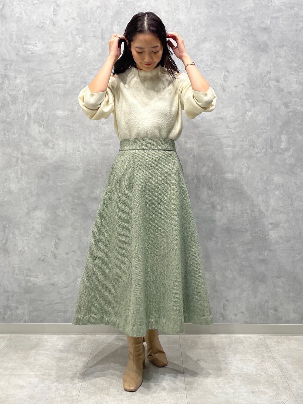 ベージュ系のブーツ、ホワイト系のニット/セーター、グリーン系のスカートを着用したレディースの冬コーディネートの2枚目の写真