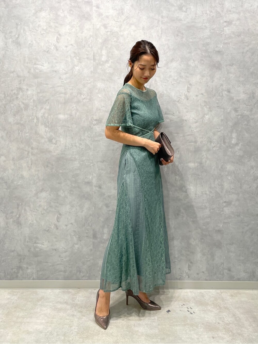 シルバー系のパンプス、シルバー系のクラッチバッグ、グリーン系のドレスを着用したレディースの夏コーディネートの4枚目の写真
