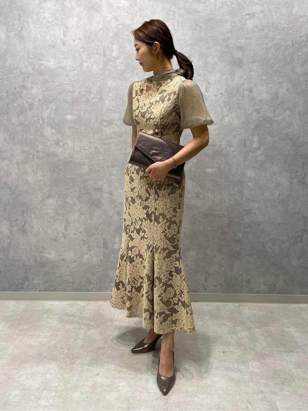 ベージュ系のドレス、シルバー系のパンプス、シルバー系のクラッチバッグを着用したレディースの夏コーディネートの2枚目の写真