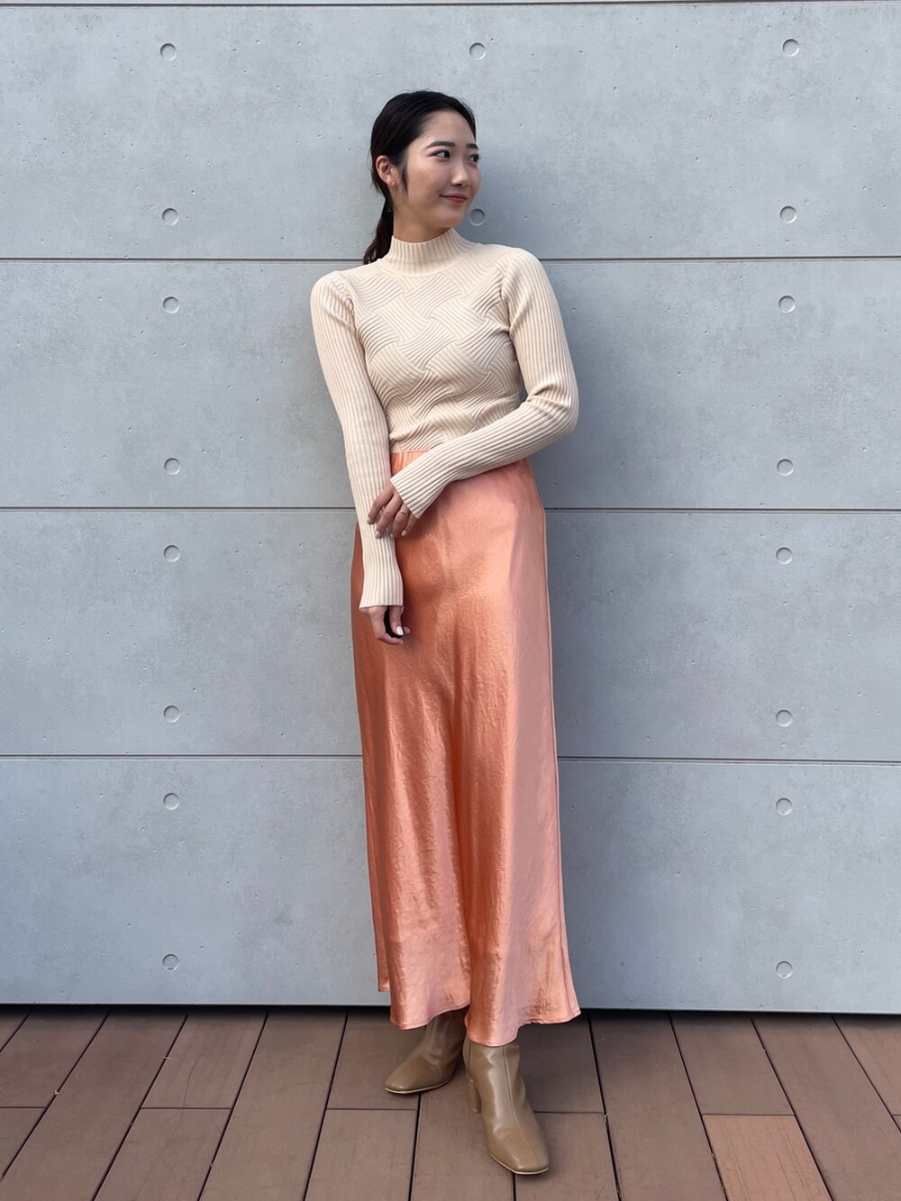 ホワイト系のニット/セーター、オレンジ系のスカート、ベージュ系のブーツを着用したレディースの冬コーディネートの2枚目の写真