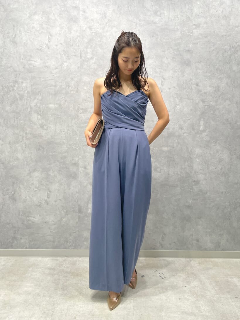 ゴールド系のパンプス、ゴールド系のクラッチバッグ、ブルー系のパンツドレスを着用したレディースの夏コーディネートの2枚目の写真