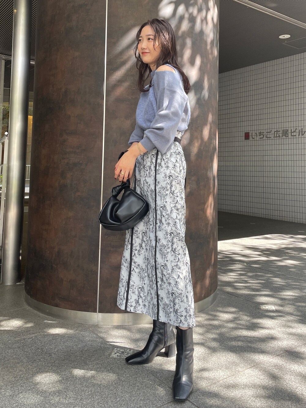 ブラック系のハンドバッグ、ブラック系のスカート、ブラック系のブーツを着用したレディースの秋コーディネートの3枚目の写真