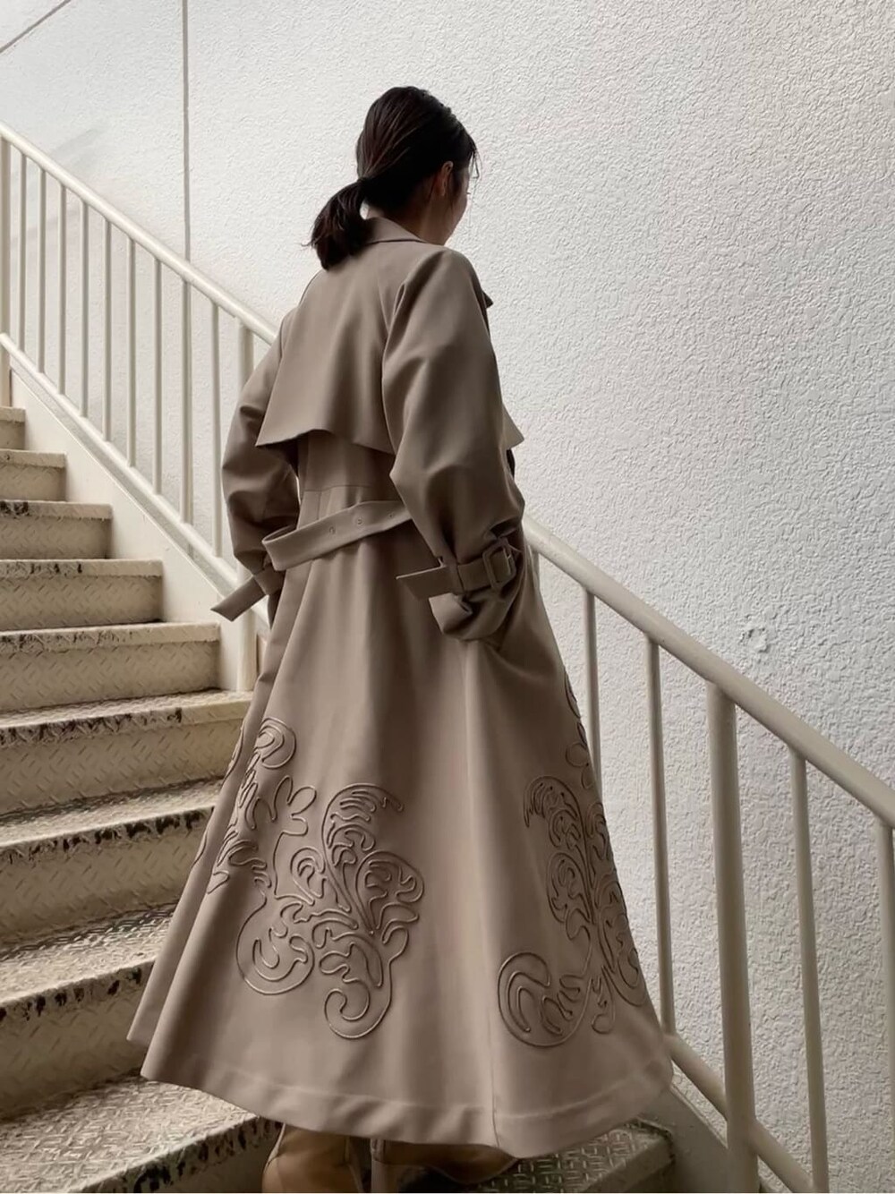 ベージュ系のトレンチコート、グレー系のワンピース、ベージュ系のブーツを着用したレディースの春コーディネートの3枚目の写真