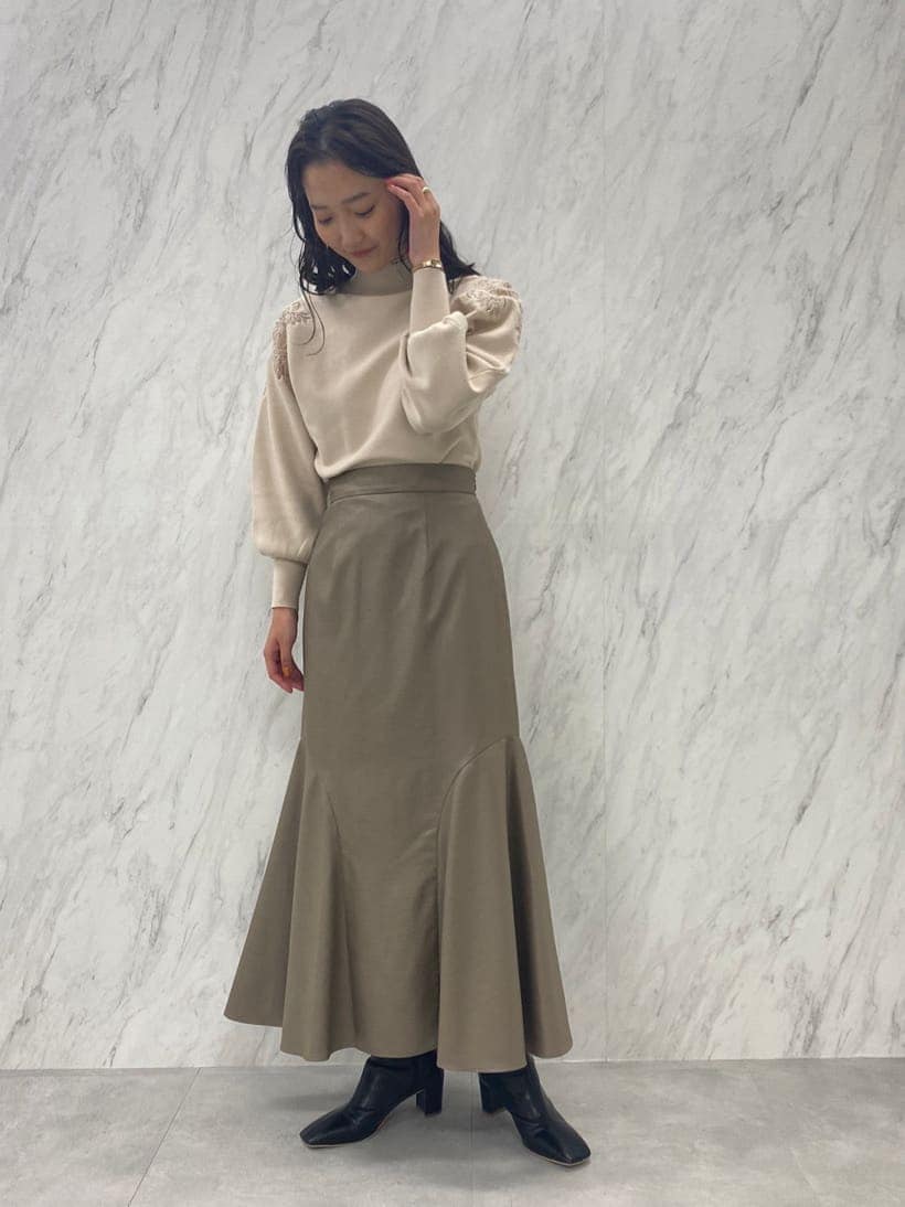 ブラック系のブーツ、ベージュ系のスカート、ホワイト系のニット/セーターを着用したレディースの秋コーディネートの3枚目の写真