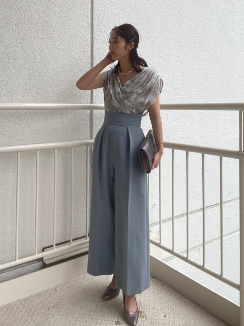 シルバー系のパンプス、シルバー系のクラッチバッグ、ブルー系のパンツドレスを着用したレディースの春コーディネートの2枚目の写真