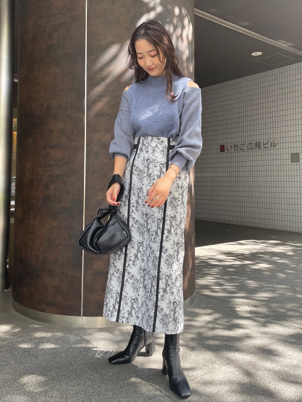 ブラック系のハンドバッグ、ブラック系のスカート、ブラック系のブーツを着用したレディースの秋コーディネートの2枚目の写真