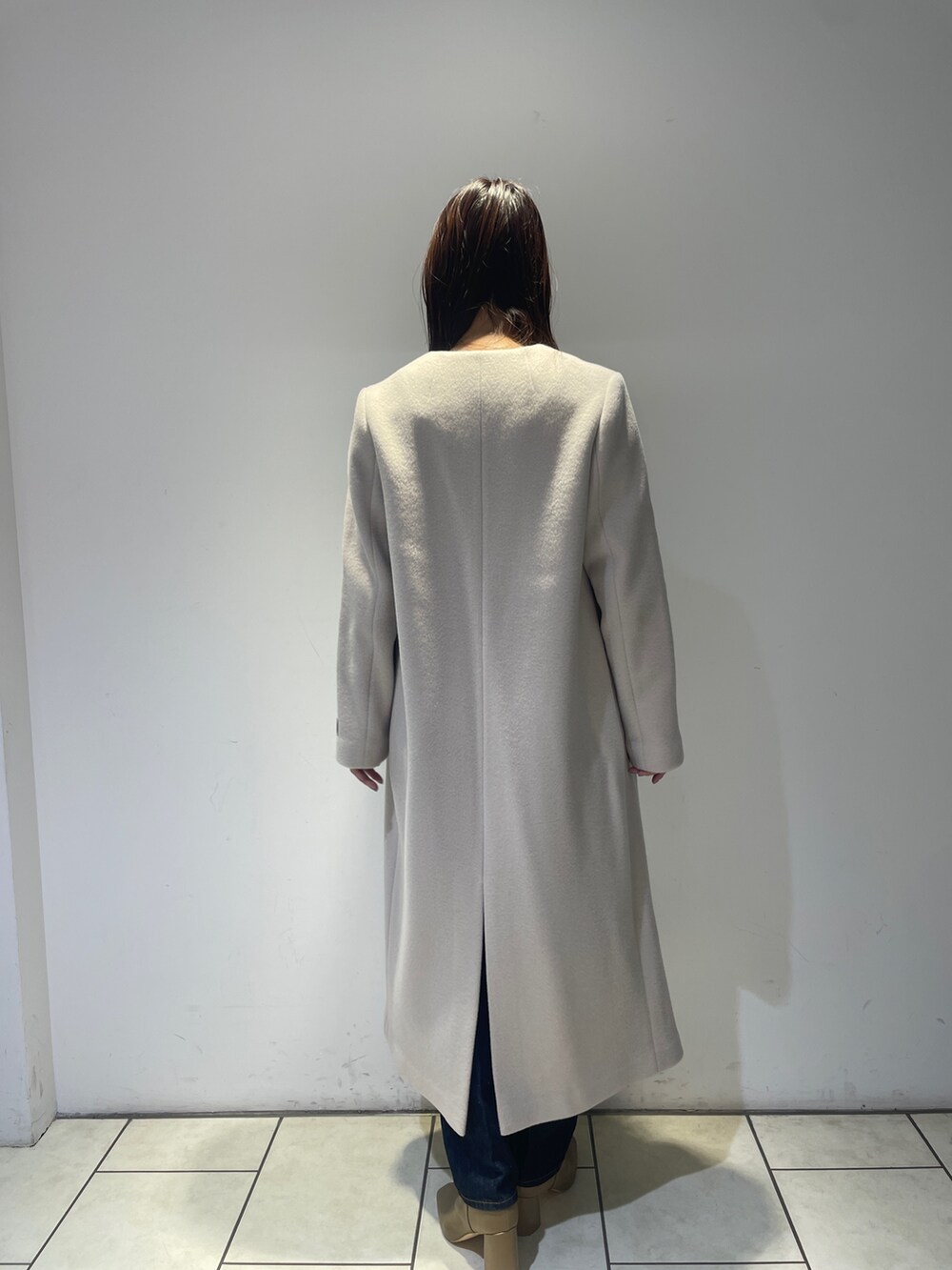 ホワイト系のノーカラーコート、グレー系のニット/セーター、ブルー系のデニムパンツを着用したレディースの秋コーディネートの3枚目の写真