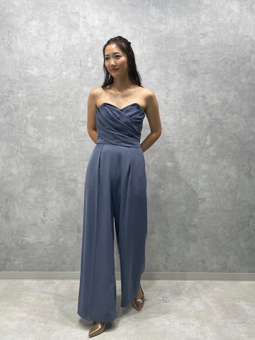 ゴールド系のパンプス、ゴールド系のクラッチバッグ、ブルー系のパンツドレスを着用したレディースの夏コーディネートの3枚目の写真