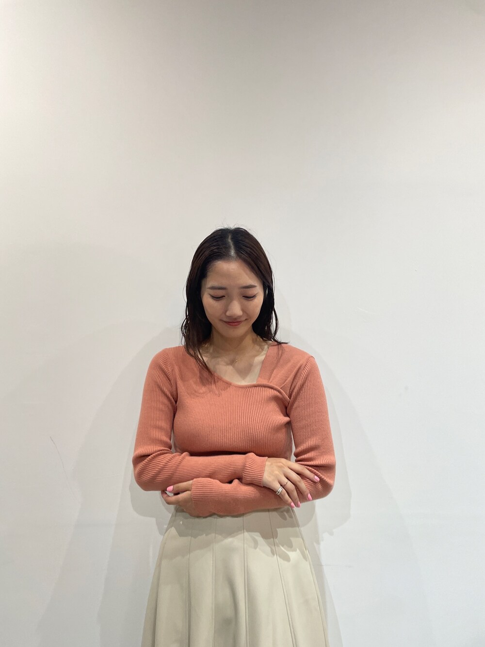 オレンジ系のニット/セーター、ホワイト系のスカート、ベージュ系のブーツを着用したレディースの夏コーディネートの6枚目の写真