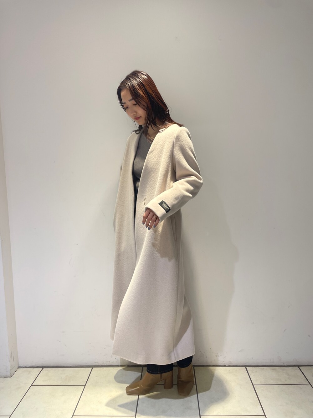 ホワイト系のノーカラーコート、グレー系のニット/セーター、ブルー系のデニムパンツを着用したレディースの秋コーディネートの2枚目の写真