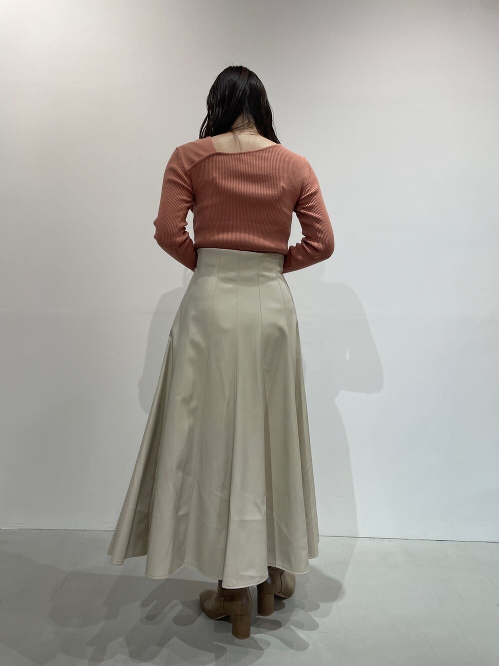 オレンジ系のニット/セーター、ホワイト系のスカート、ベージュ系のブーツを着用したレディースの夏コーディネートの4枚目の写真