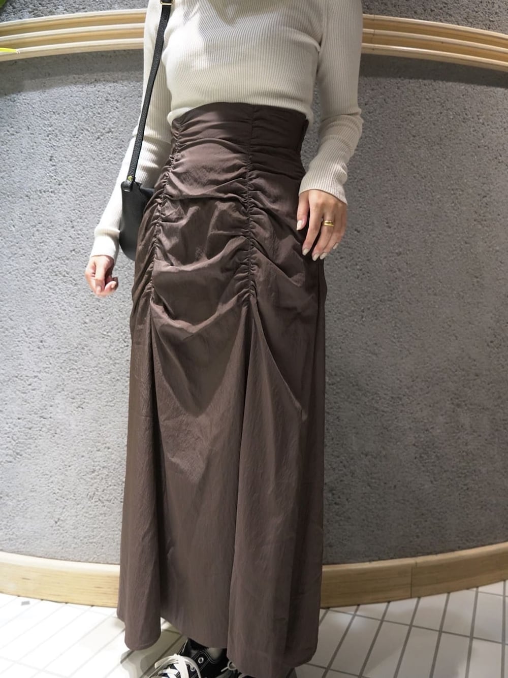 ブラック系のショルダーバッグ、ブラウン系のスカート、ホワイト系のニット/セーターを着用したレディースの秋コーディネートの5枚目の写真