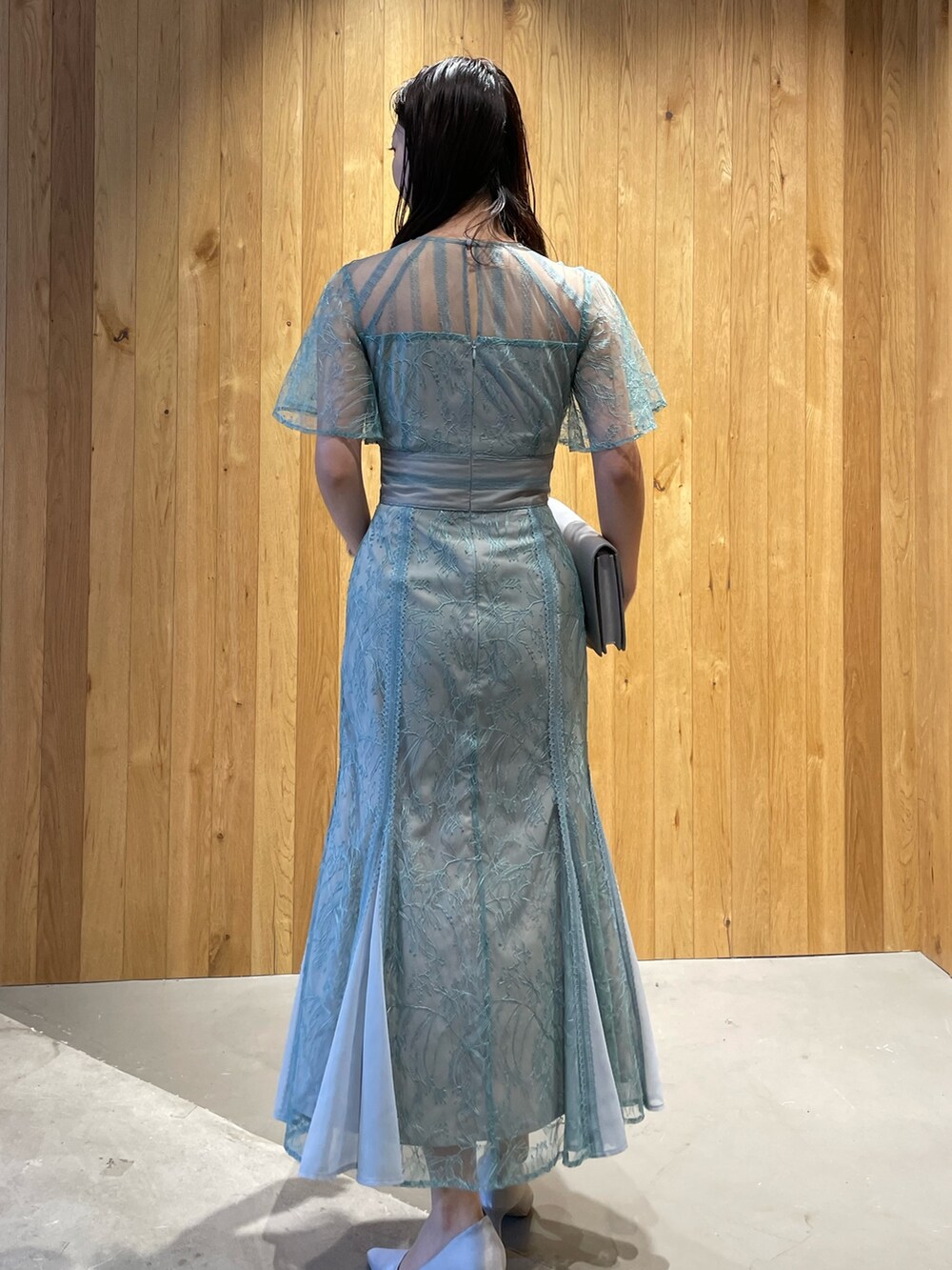 グレー系のクラッチバッグ、グレー系のパンプス、グリーン系のドレスを着用したレディースの冬コーディネートの4枚目の写真