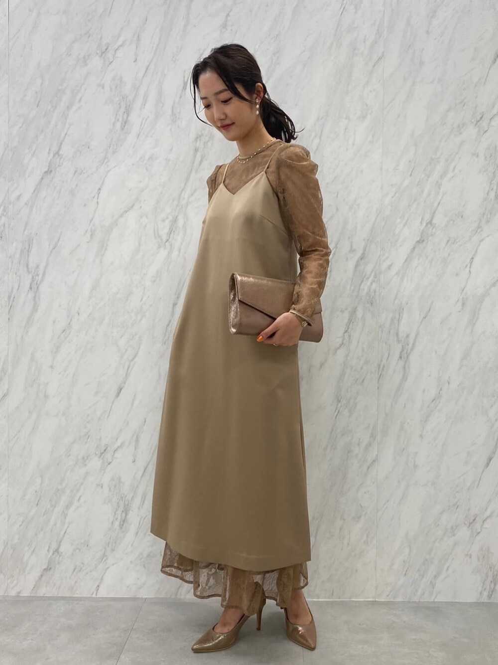 ゴールド系のパンプス、ゴールド系のクラッチバッグ、ベージュ系のドレスを着用したレディースの夏コーディネートの7枚目の写真