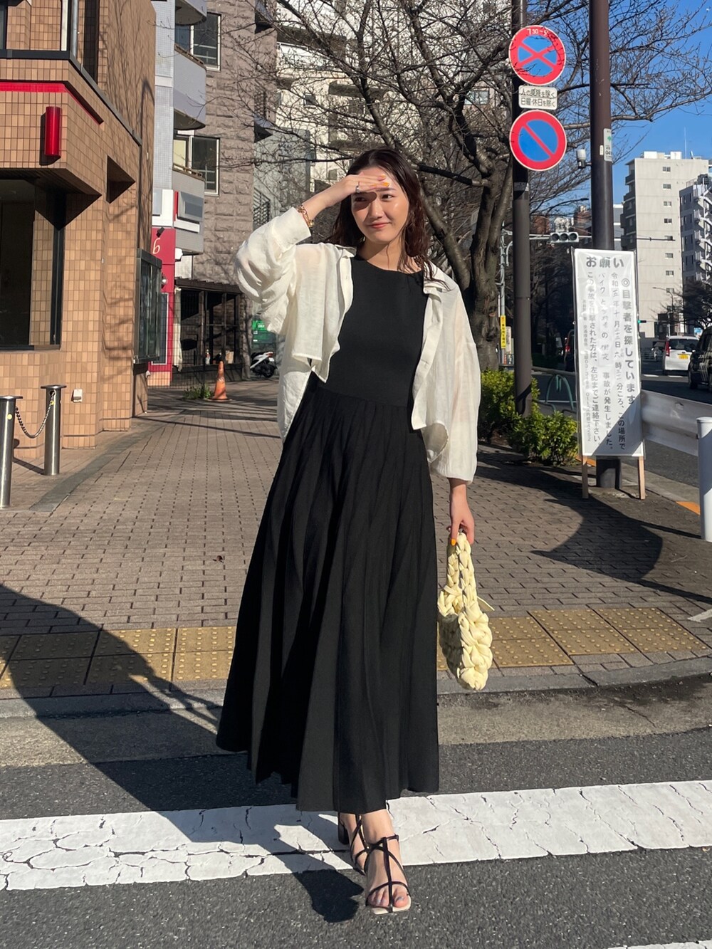 ブラック系のワンピース、ベージュ系のハンドバッグ、ブラック系のサンダルを着用したレディースの春コーディネートの5枚目の写真