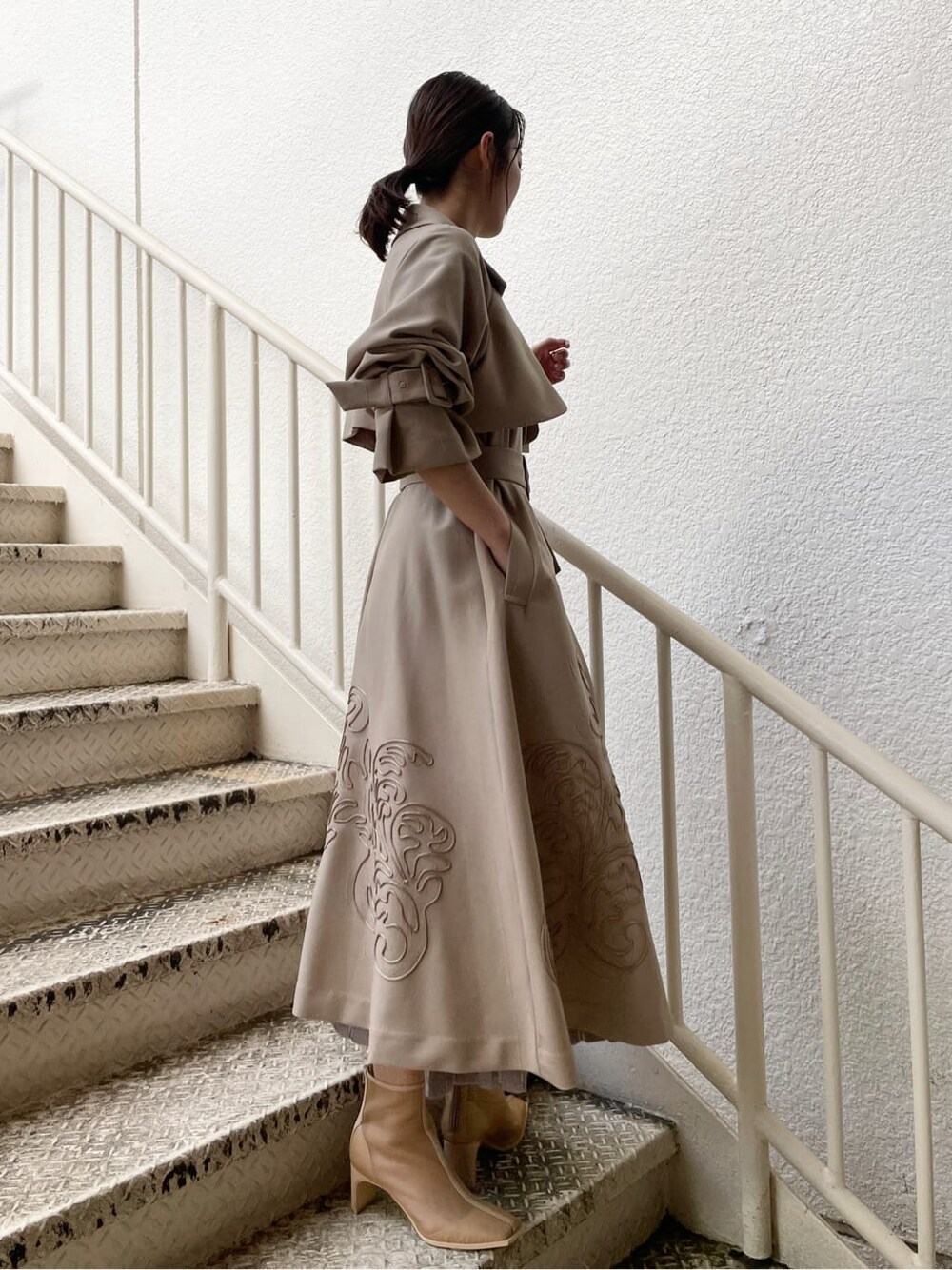 ベージュ系のトレンチコート、グレー系のワンピース、ベージュ系のブーツを着用したレディースの春コーディネートの2枚目の写真