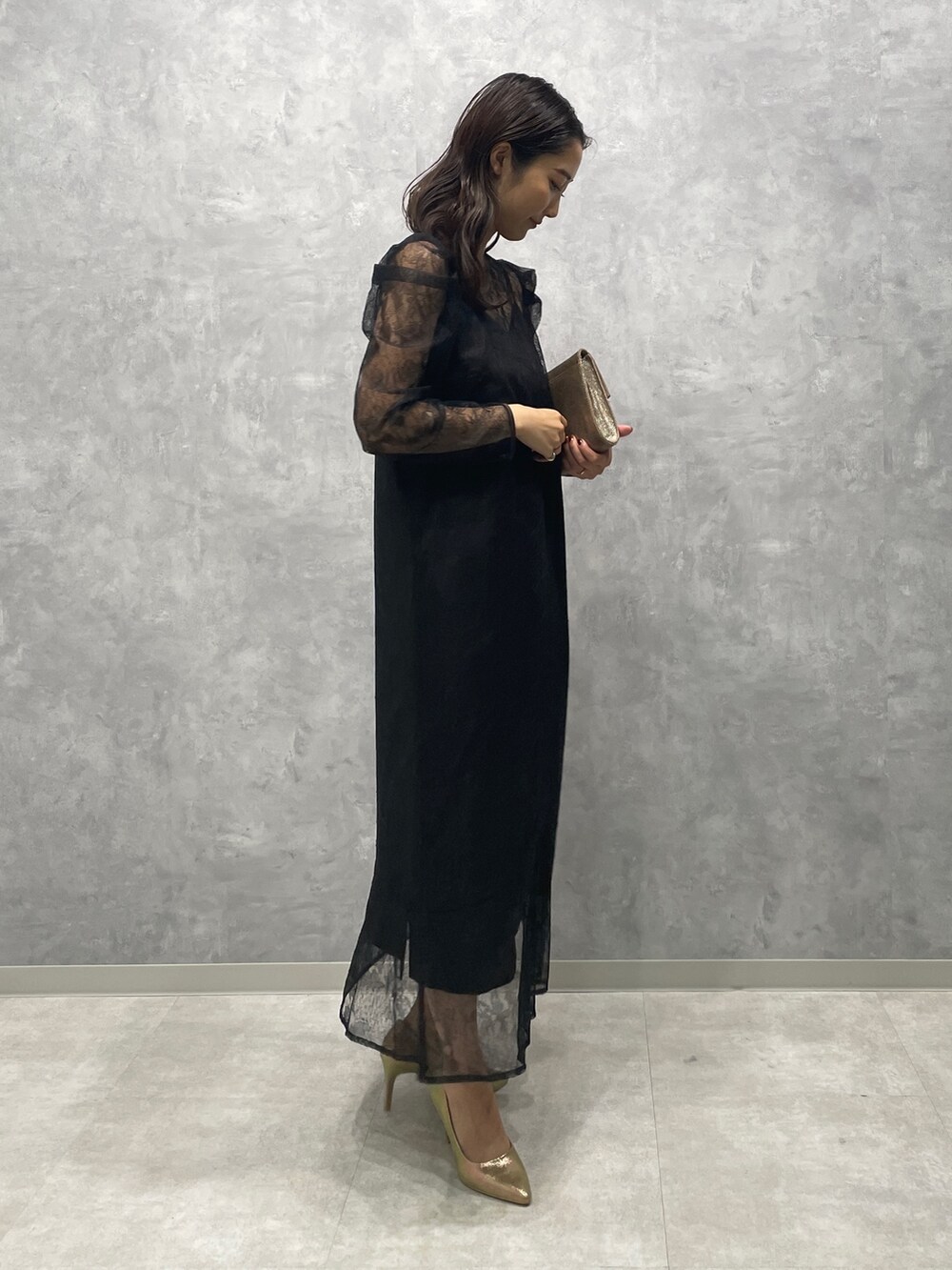 ゴールド系のパンプス、ゴールド系のハンドバッグ、ブラック系のドレスを着用したレディースの秋コーディネートの4枚目の写真