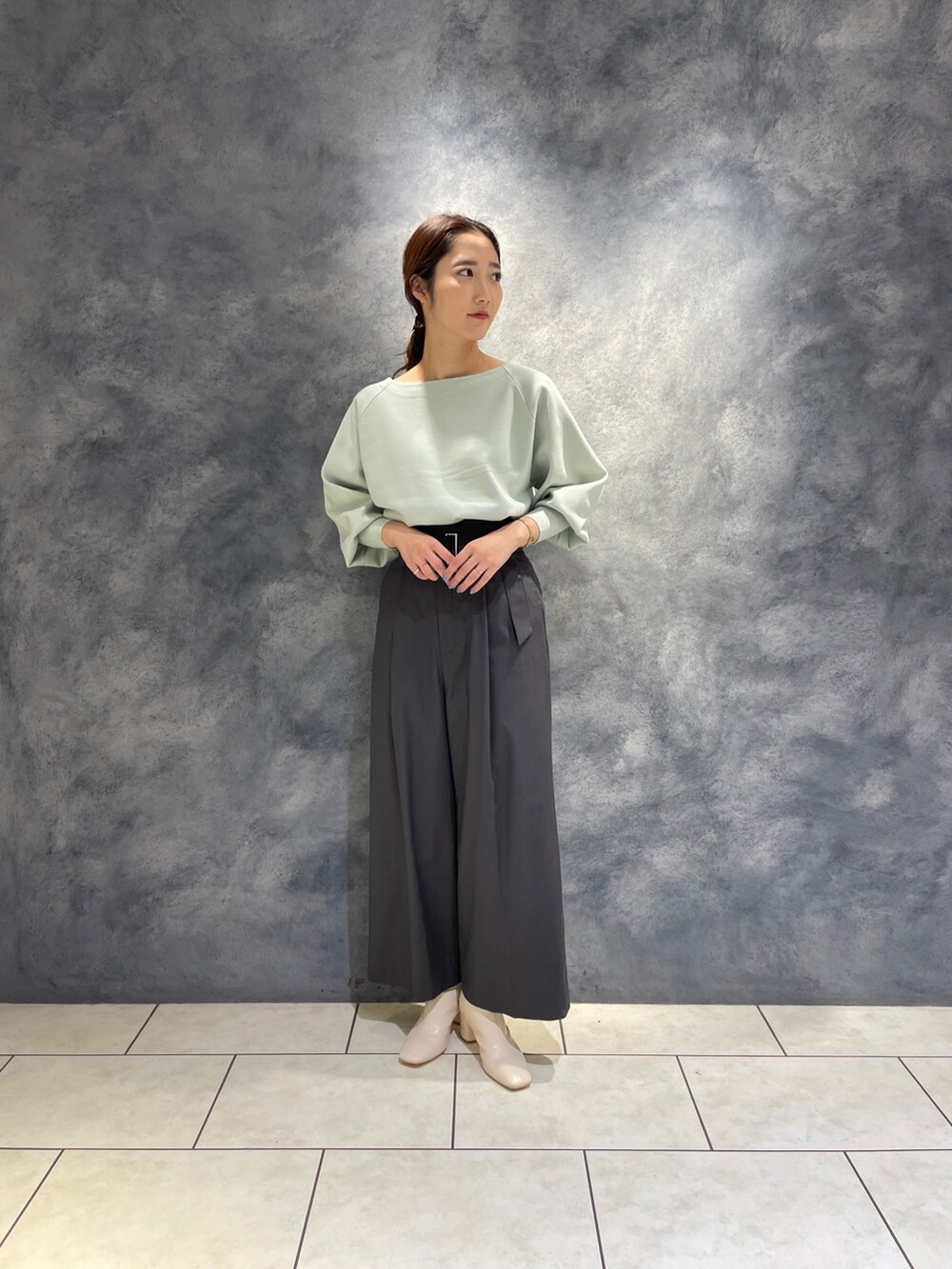 グレー系のその他パンツ、ホワイト系のブーツ、グリーン系のニット/セーターを着用したレディースの冬コーディネートの3枚目の写真