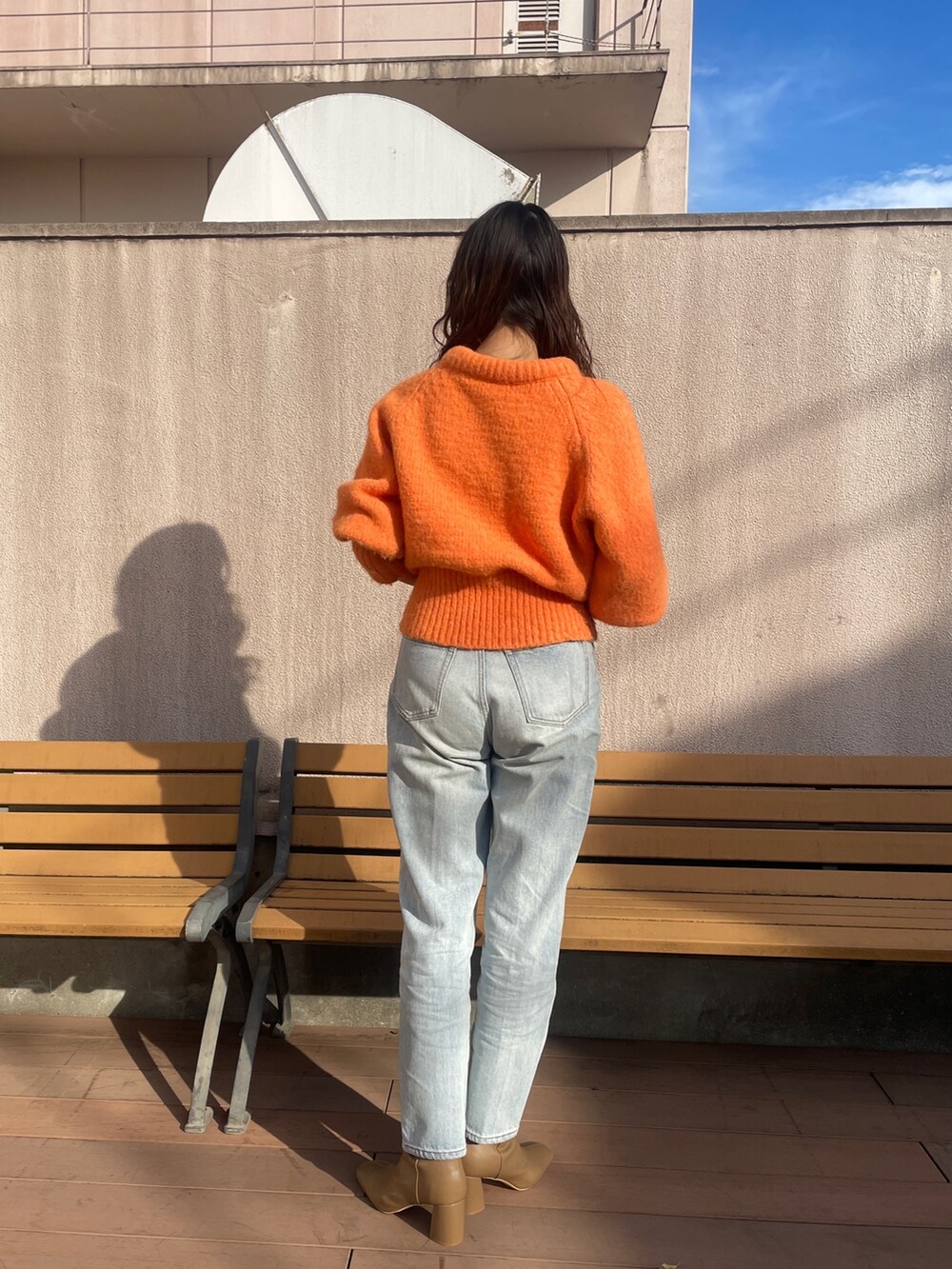 ブルー系のデニムパンツ、オレンジ系のニット/セーター、ベージュ系のブーツを着用したレディースの冬コーディネートの3枚目の写真