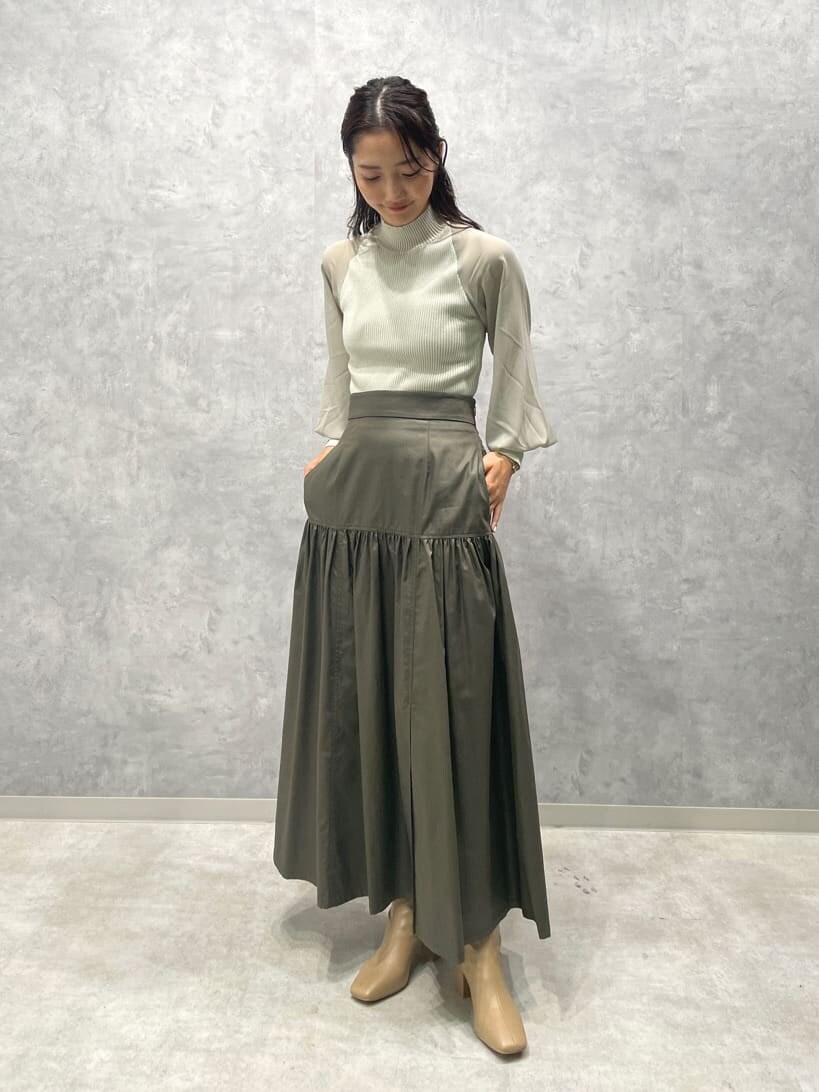 ベージュ系のスカート、ベージュ系のブーツ、グリーン系のニット/セーターを着用したレディースの夏コーディネートの2枚目の写真