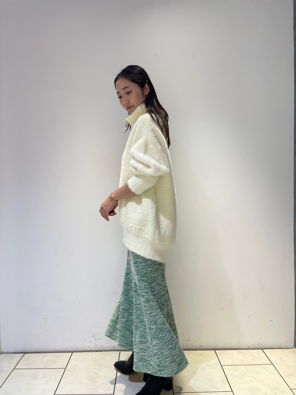 ホワイト系のニット/セーター、ブラック系のブーツ、グリーン系のスカートを着用したレディースの秋コーディネートの4枚目の写真