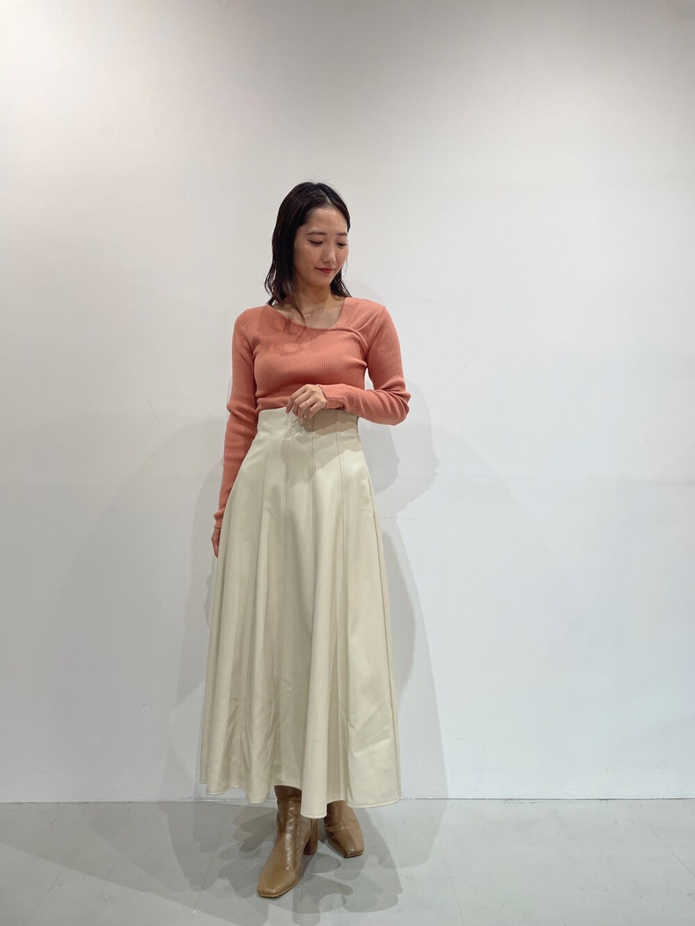 オレンジ系のニット/セーター、ホワイト系のスカート、ベージュ系のブーツを着用したレディースの秋コーディネートの3枚目の写真