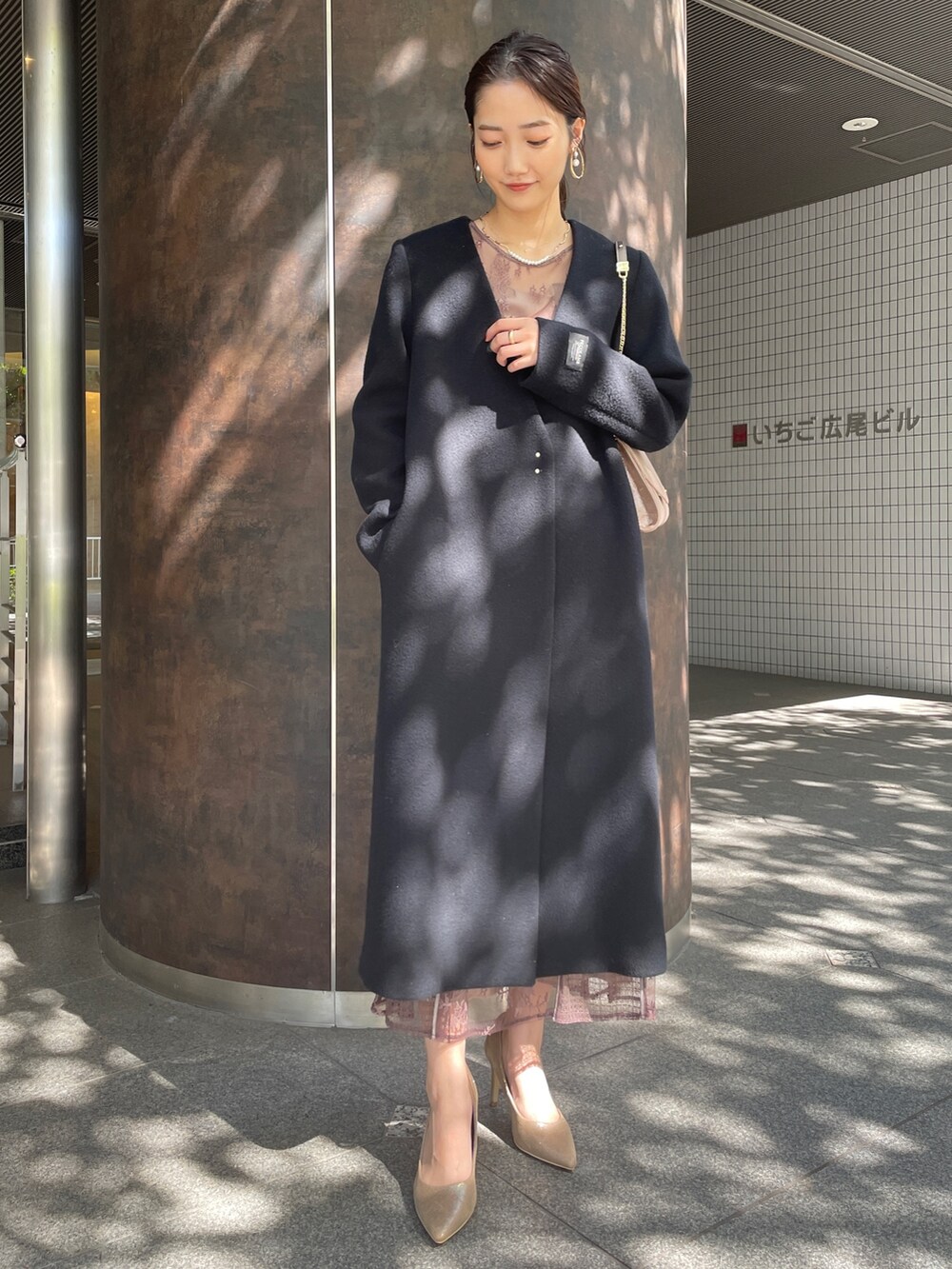 ベージュ系のドレス、ブラック系のノーカラーコート、ゴールド系のハンドバッグを着用したレディースの秋コーディネートの2枚目の写真