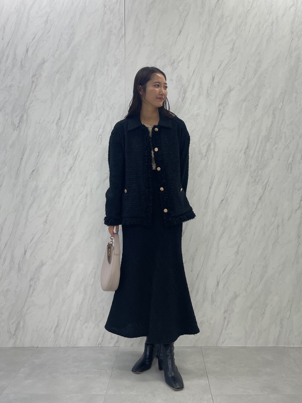 ブラック系のブーツ、ホワイト系のハンドバッグ、ブラック系のスカートを着用したレディースの秋コーディネートの2枚目の写真